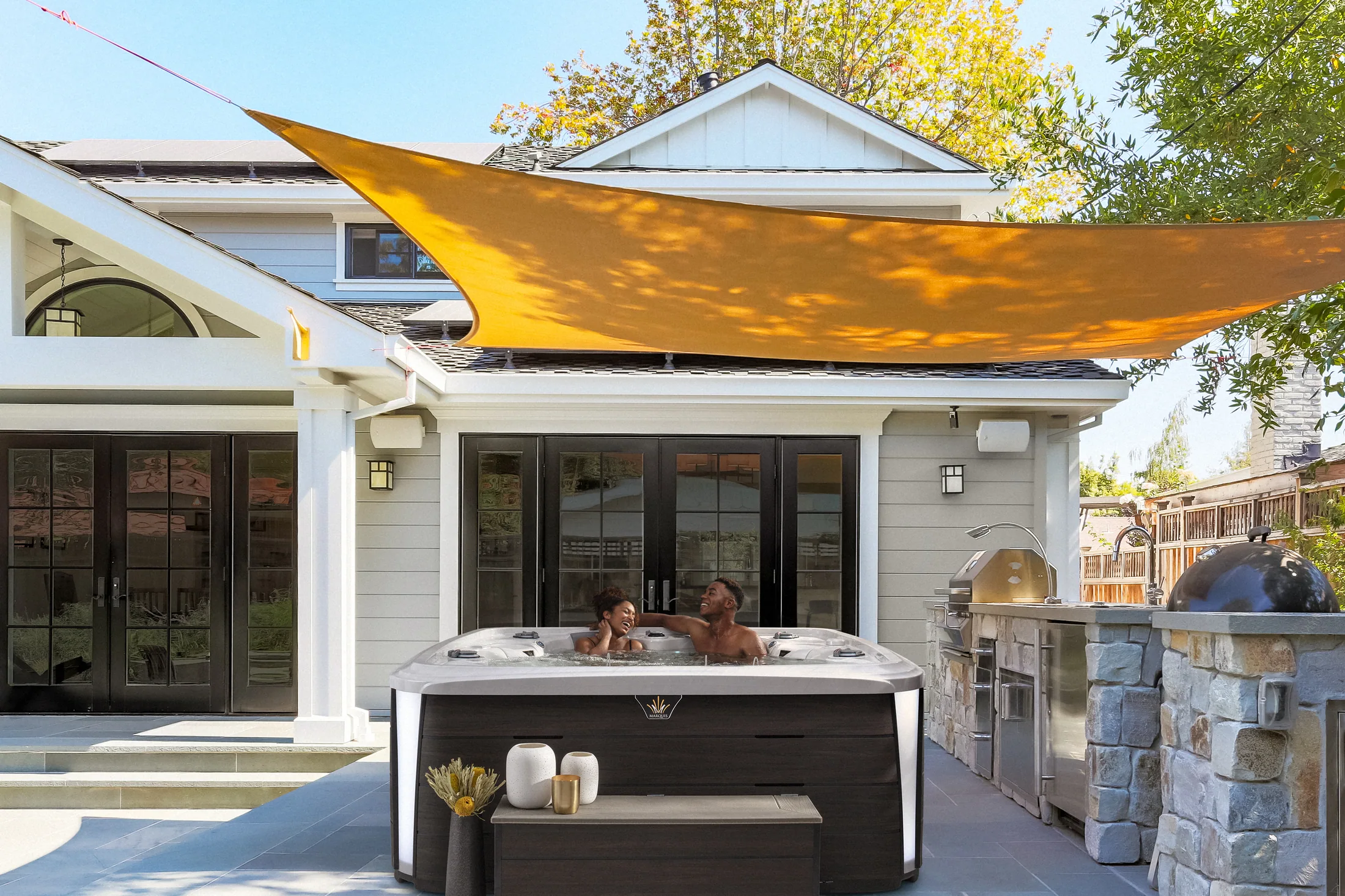 Outdoor hot tub below a shade canopy beside a home